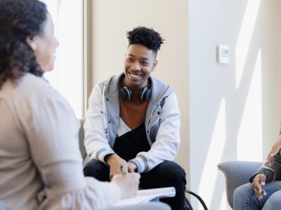 The young adult is smiling while listening to his mentor encourage him.