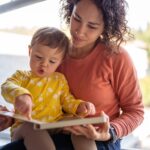 Affectionate mother reading book with adorable toddler daughter