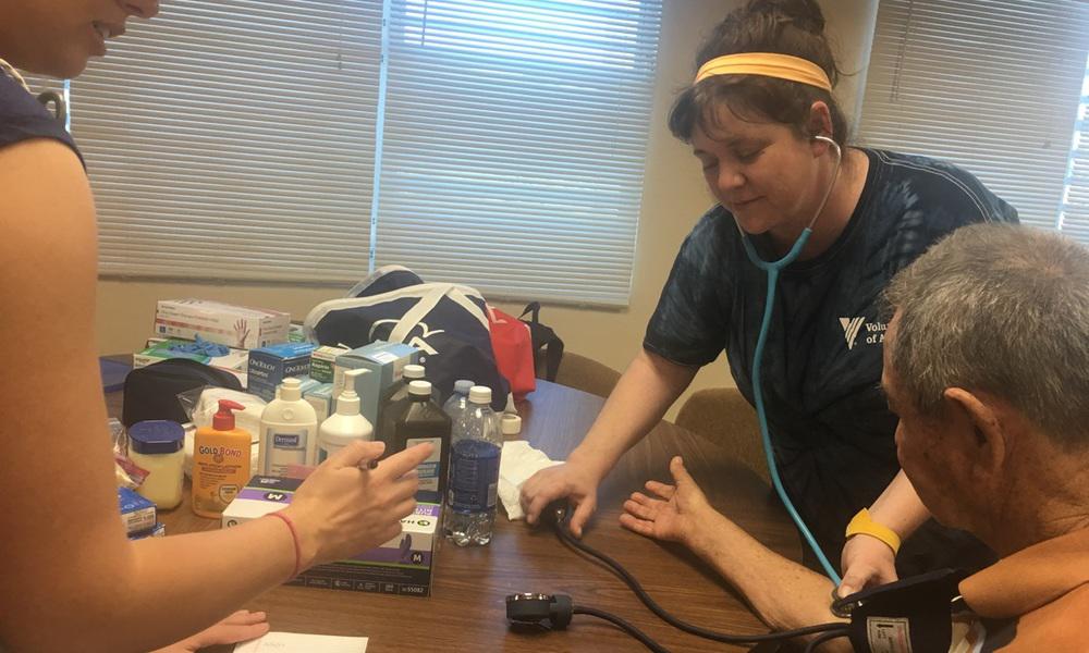 a volunteer woman takes an older man's blood pressure at puerto rico project esperanza setup