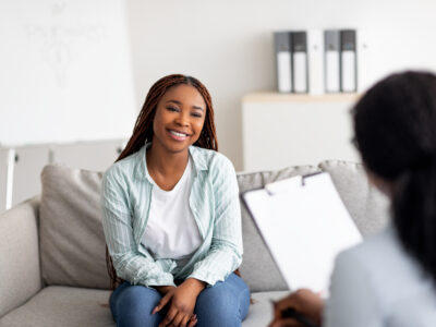 Successful therapy. Young female client having consultation with psychologist, grateful for professional help at clinic. Happy black lady speaking with her psychotherapist, solving emotional problem