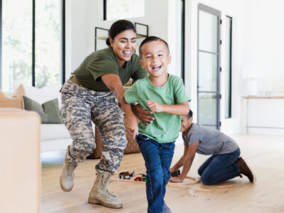 While the preteen boy sets up the wooden train set on the living room floor, the female soldier chases the elementary age boy through the house.  Everybody is smiling and happy.