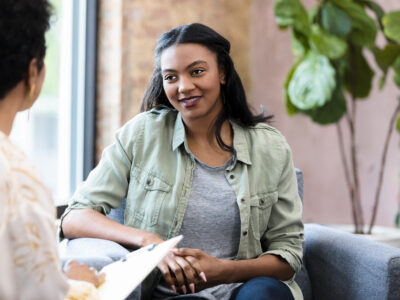 The young adult woman seems hopeful as she listens to the unrecognizable female therapist.