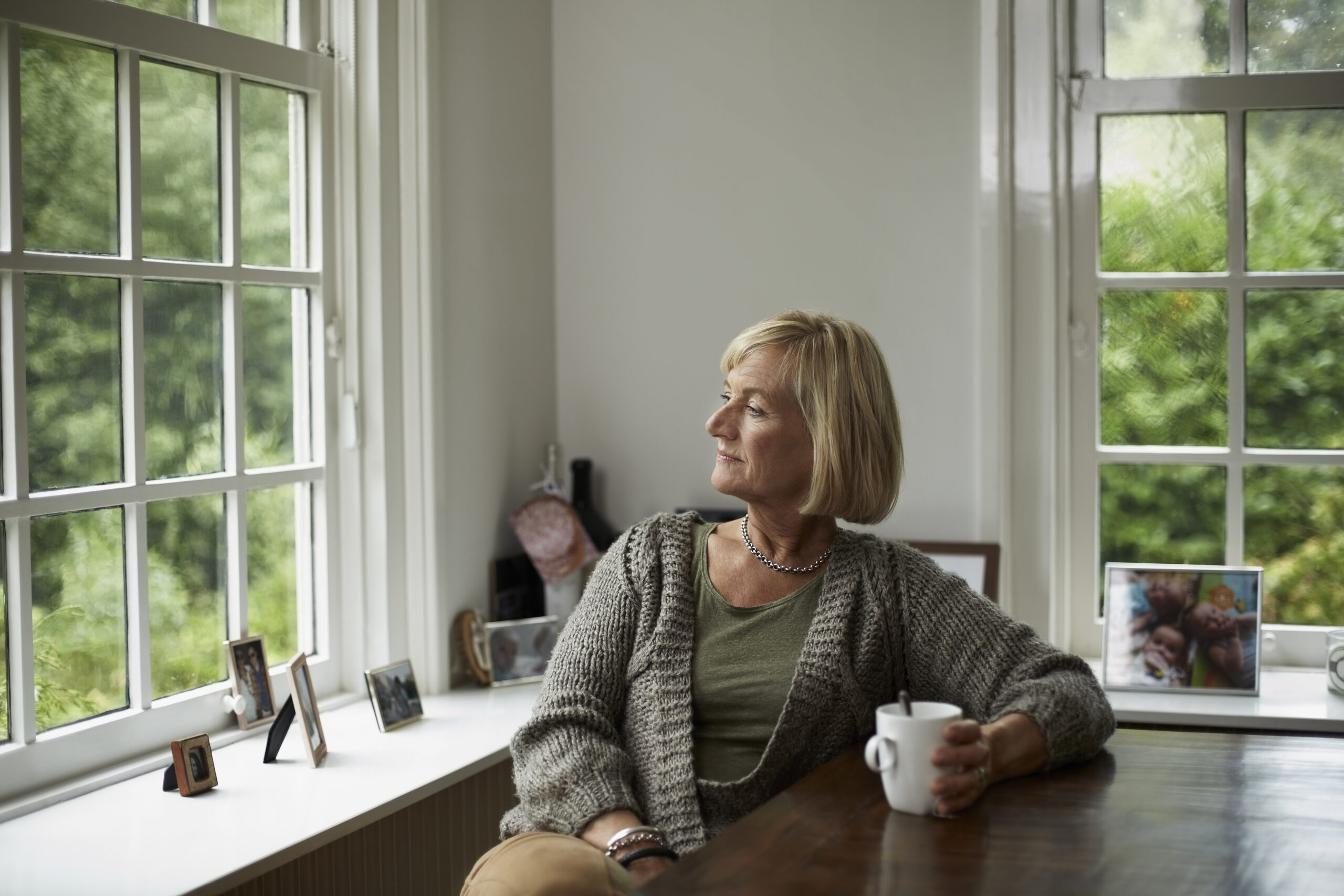 Thoughtful senior woman having coffee at table in cottage