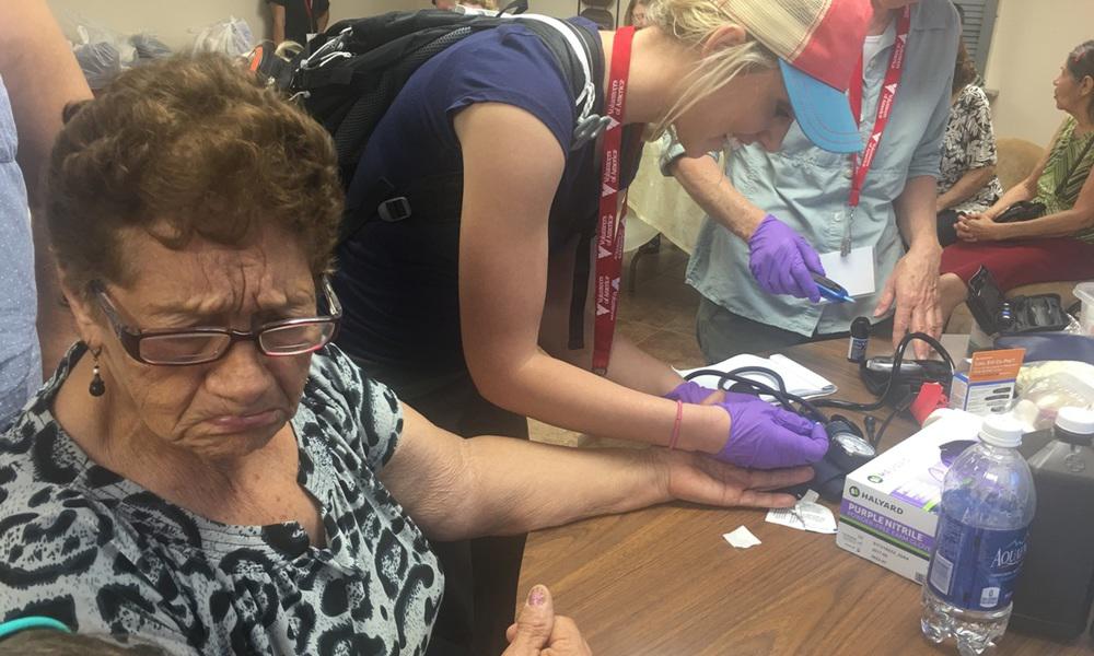 a volunteer young woman takes a test sample of an older lady's blood at puerto rico project esperanza setup