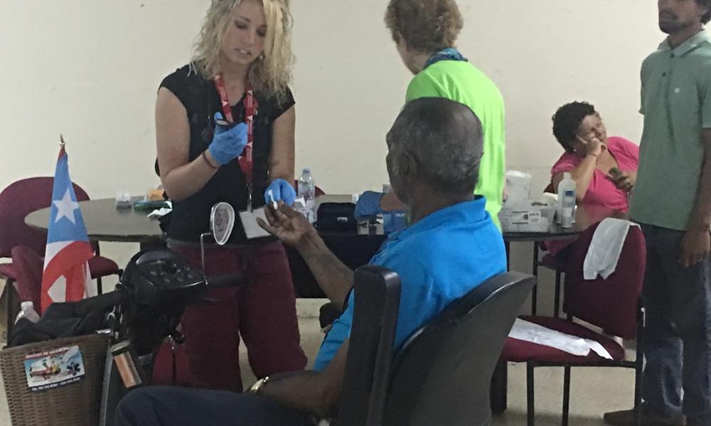 a volunteer young woman takes a test sample of an older man's blood at puerto rico project esperanza setup