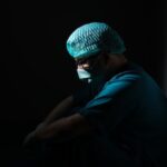 doctor in scrubs in spotlight resting against wall