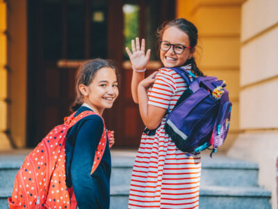 two girls smiling and wave as they walk into school