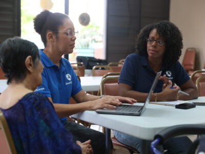 woman typing on keyboard with two people sitting beside her at a table