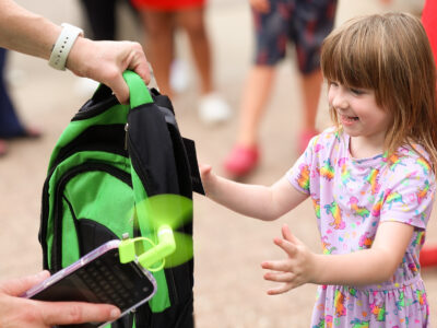 little girl opening hands to receive green backpack at event